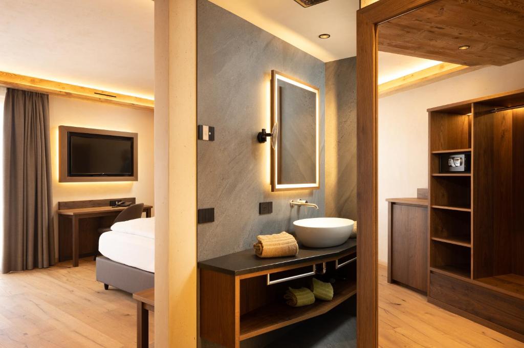 a bathroom with a sink and a bed and a television at Camino Rustic Chic Hotel in Livigno