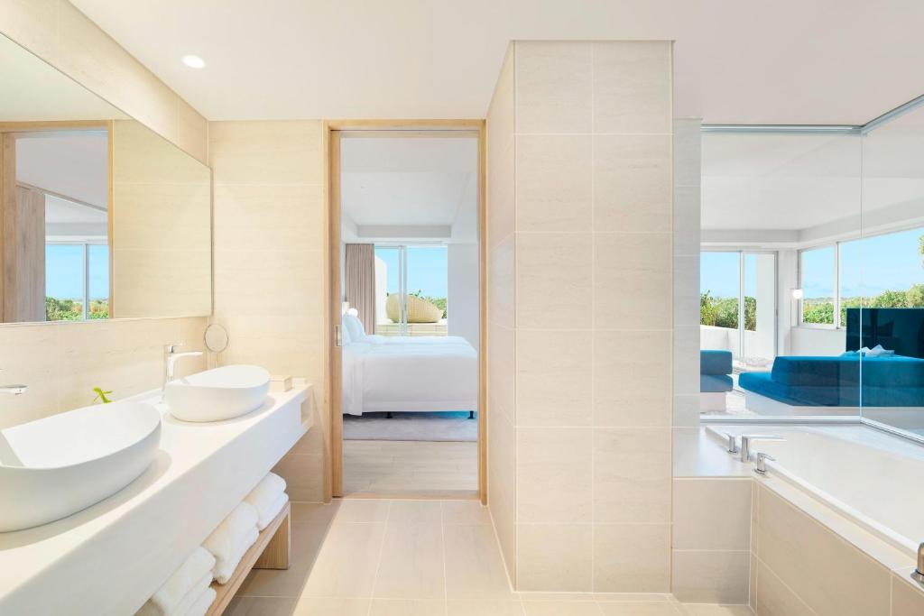 a bathroom with two sinks and a tub and a bedroom at IRAPH SUI, a Luxury Collection Hotel, Miyako Okinawa in Miyako-jima