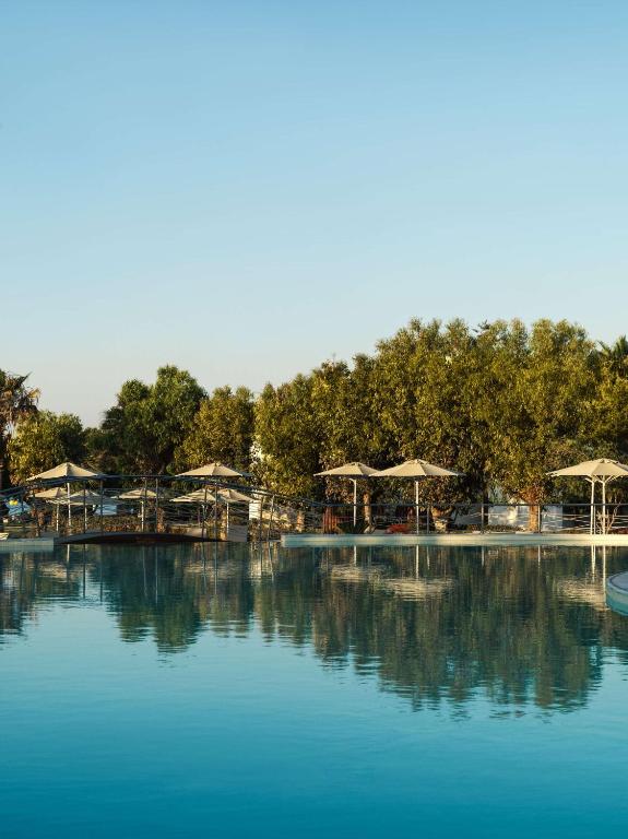 a large pool of water with umbrellas and trees at Lindian Village All Inclusive Resort Rhodes,Curio Collection in Kiotari