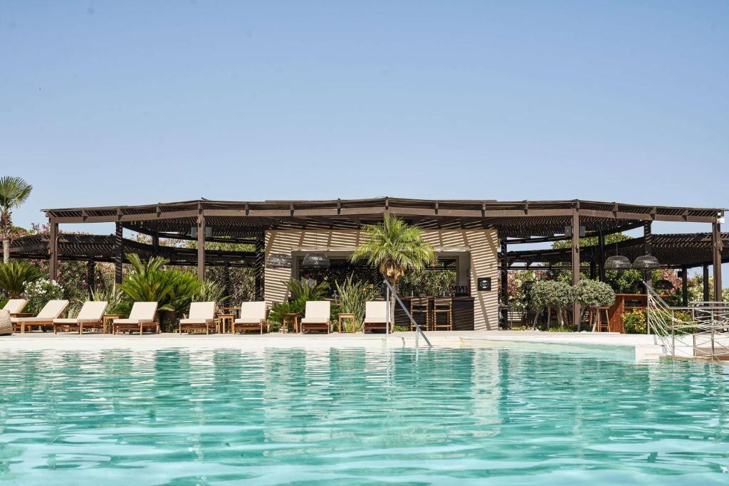 a swimming pool with chairs and a building at Lindian Village All Inclusive Resort Rhodes,Curio Collection in Kiotari