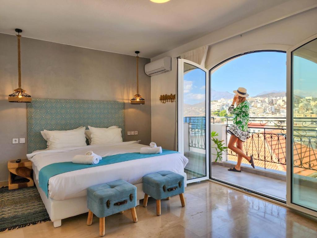 a bedroom with a bed and a woman walking on a balcony at Hotel Port 7- Boutique Collection in Agios Nikolaos