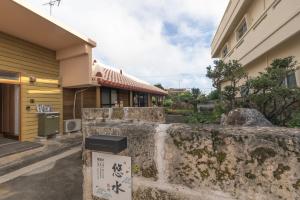 a stone wall with a sign in front of a building at 田舎の静かな古民家の悠水居 in Itoman