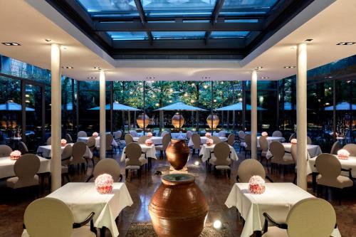a restaurant with white tables and chairs and large windows at The Mandala Berlin, a Member of Design Hotels in Berlin